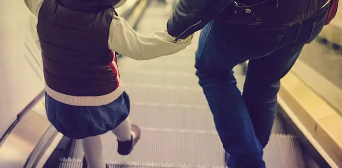 Father holding hands with his young daughter walking down an escalator.