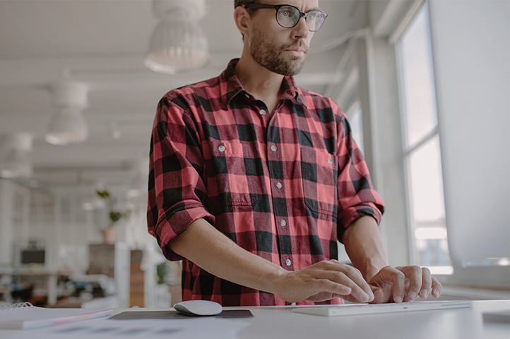 Man wearing plaid shirt tying at a computer.