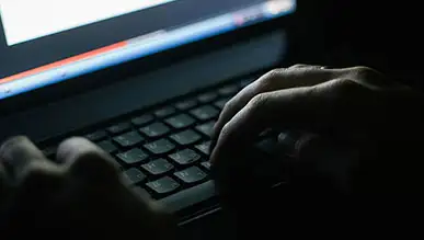 A person typing on a laptop in the dark.