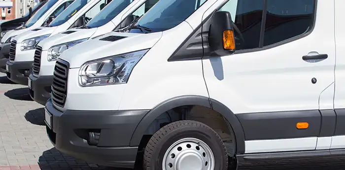 A row of white cargo vans parked in a lot.