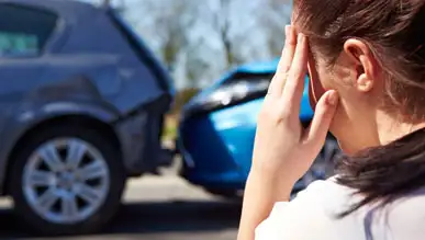 A woman holding her hand against her head after a car accident, with cars in the background.