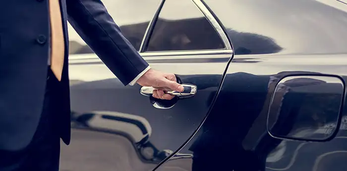 Man in a suit opening the door of a black car.